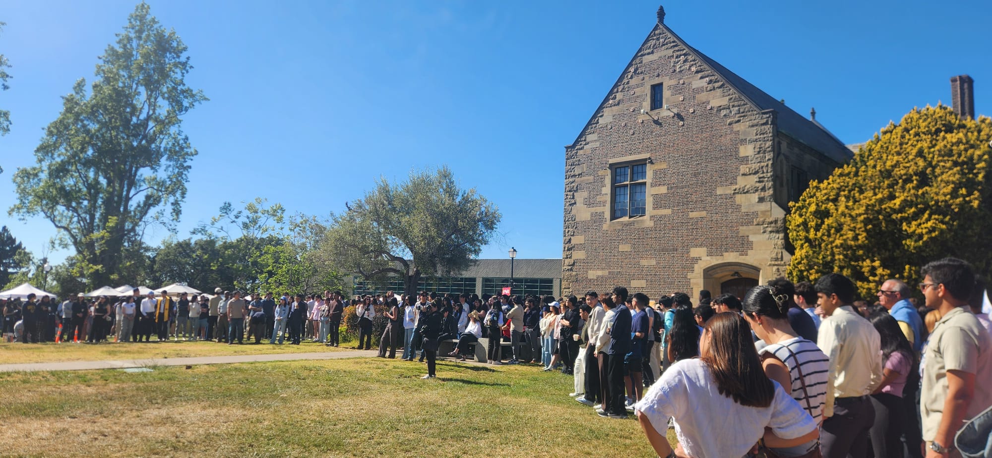 A semi-circle of people standing around a lawn at the Fung Institute End of Year Showcase 2025.